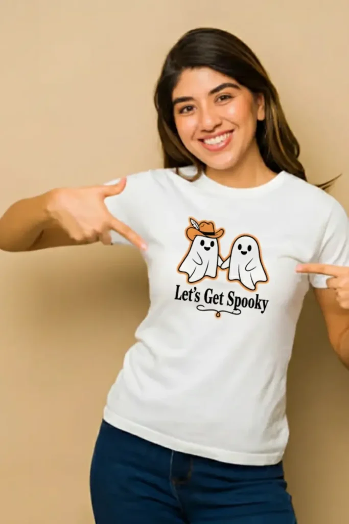 A smiling woman pointing to her white t-shirt, which features a 'Spooky Date Night' fall t-shirt design of two cute cartoon ghosts, created to show how to make money with AI.